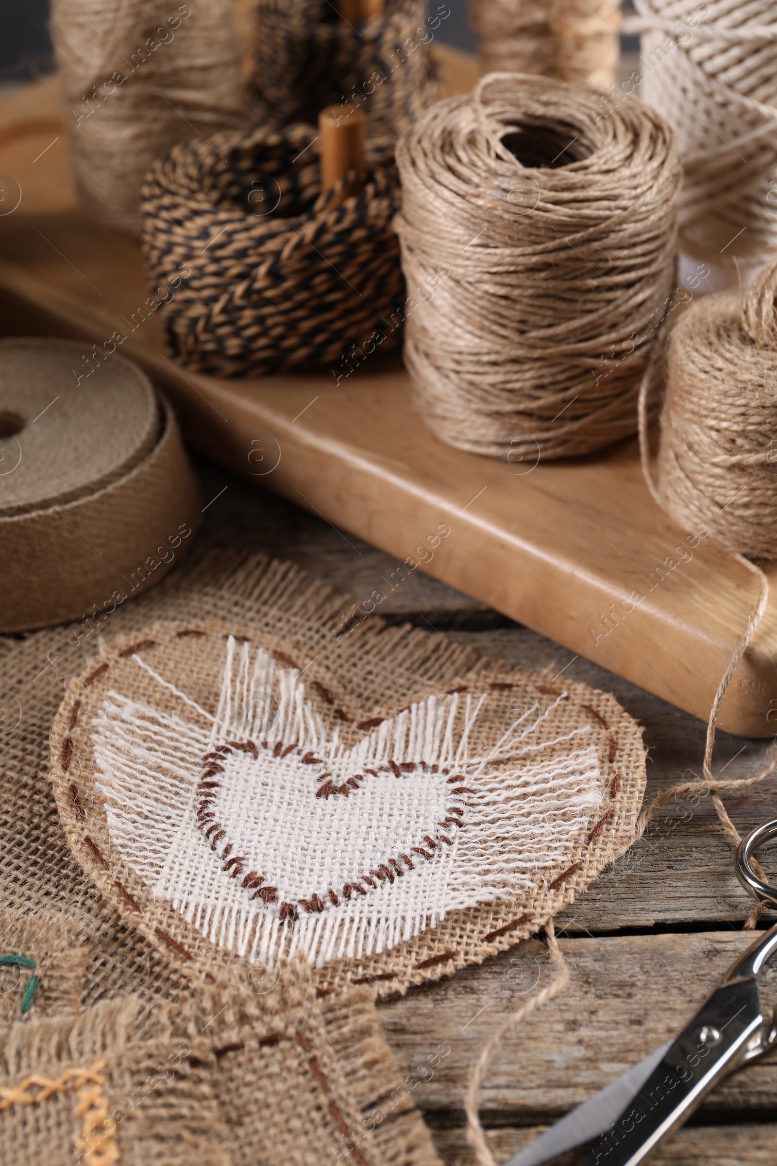 Photo of Heart of burlap fabric with stitches and spools of twine on wooden table