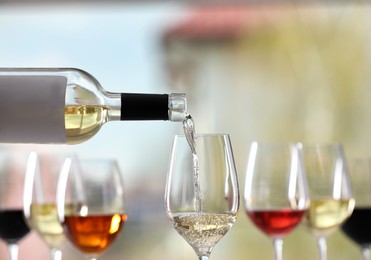 Pouring white wine from bottle into glass on blurred background, closeup