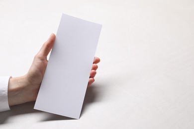 Woman holding blank card at white table, closeup. Mockup for design