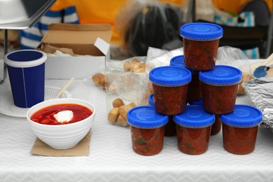Volunteer food distribution. Containers with tasty adjika sauce near bowl of borsch served on table outdoors