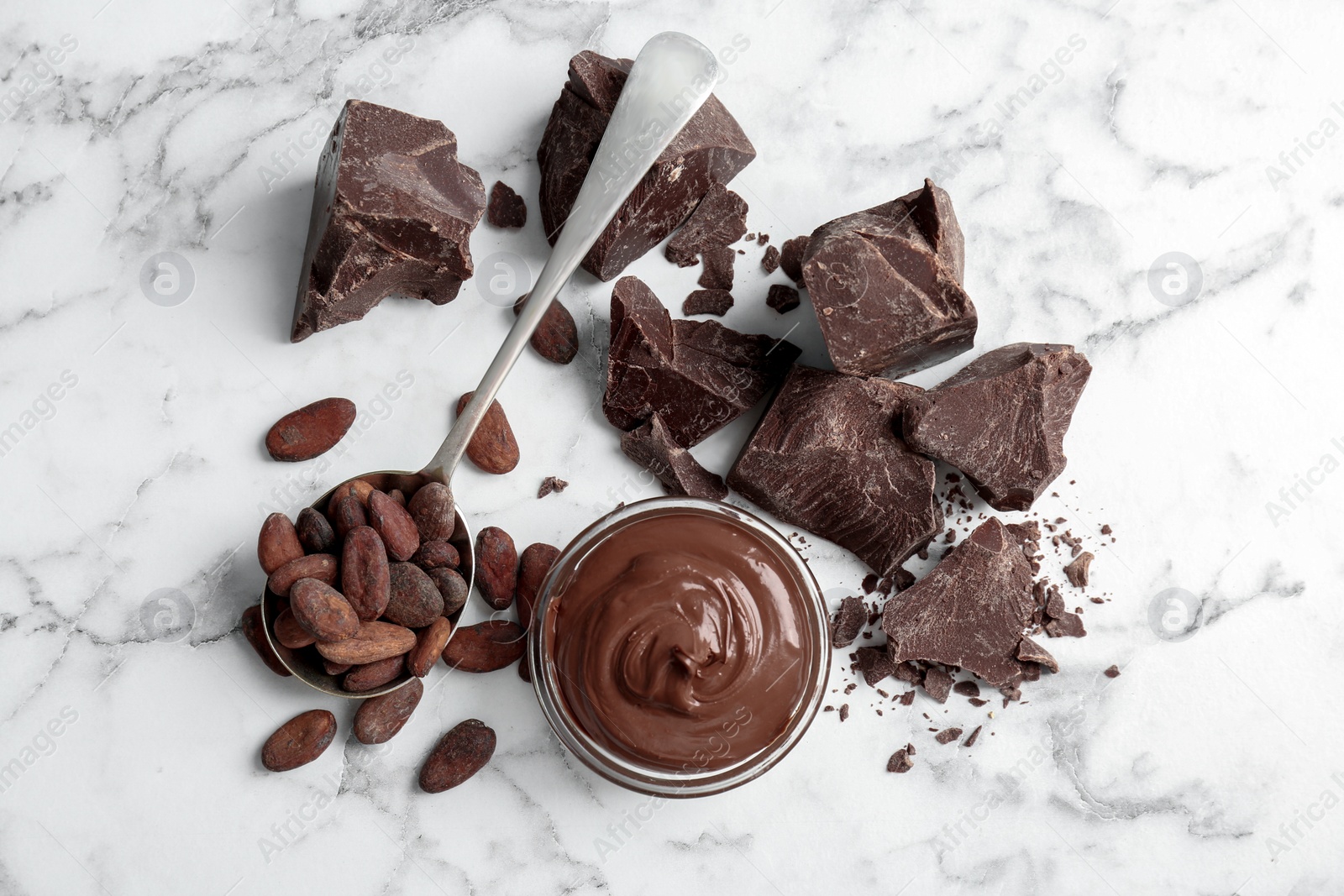 Photo of Bowl with tasty melted chocolate, chunks and cocoa beans on table, top view