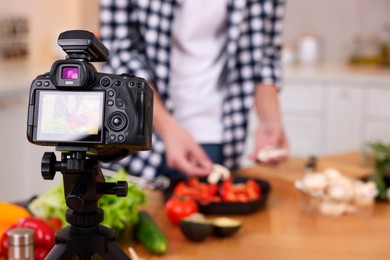 Photo of Food blogger cooking while recording video in kitchen, focus on camera