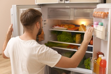 Photo of Young man choosing food in refrigerator at home