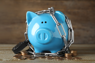 Piggy bank with steel chain, padlock and coins on wooden table. Money safety concept