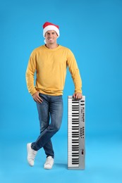 Photo of Man in Santa hat with synthesizer on light blue background. Christmas music