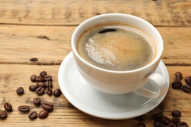 Cup of aromatic coffee and beans on wooden table, closeup