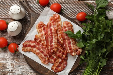 Photo of Fried bacon slices, tomatoes, parsley and spices on wooden rustic table, flat lay