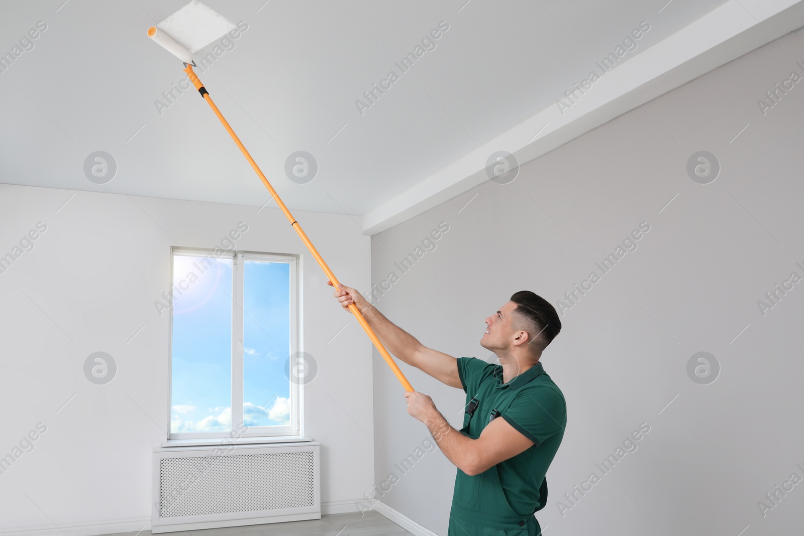 Photo of Man painting ceiling with roller in room