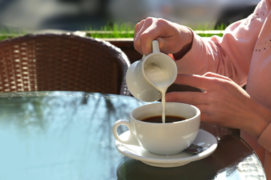 Photo of Woman pouring milk in coffee at table in cafe