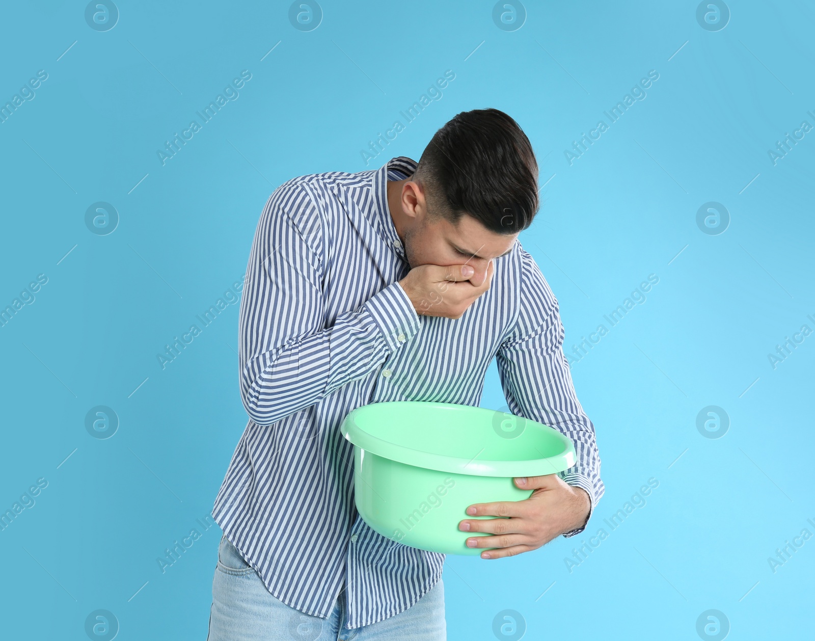 Photo of Man with basin suffering from nausea on light blue background. Food poisoning