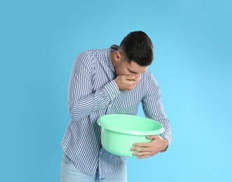 Photo of Man with basin suffering from nausea on light blue background. Food poisoning