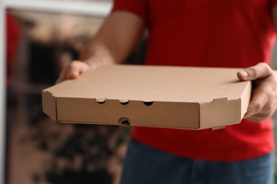 Photo of Courier with pizza box on blurred background, closeup. Space for text