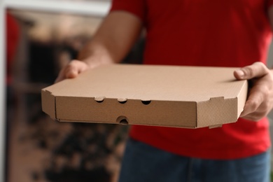 Courier with pizza box on blurred background, closeup. Space for text