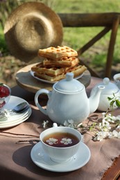 Photo of Beautiful spring flowers and freshly baked waffles on table served for tea drinking in garden