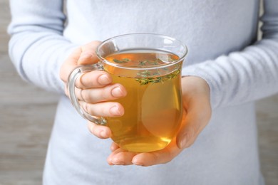 Photo of Woman holding cup of tasty herbal tea with thyme, closeup