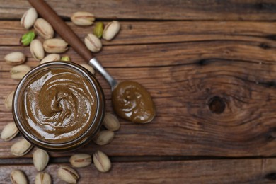 Tasty pistachio nut paste in jar and spoon on wooden table, flat lay. Space for text