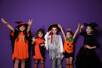 Photo of Cute little kids wearing Halloween costumes on purple background