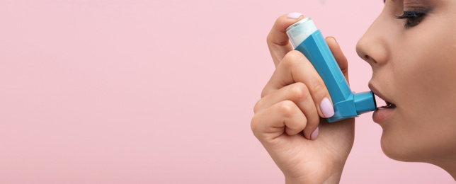 Image of Young woman using asthma inhaler on pink background, space for text. Banner design