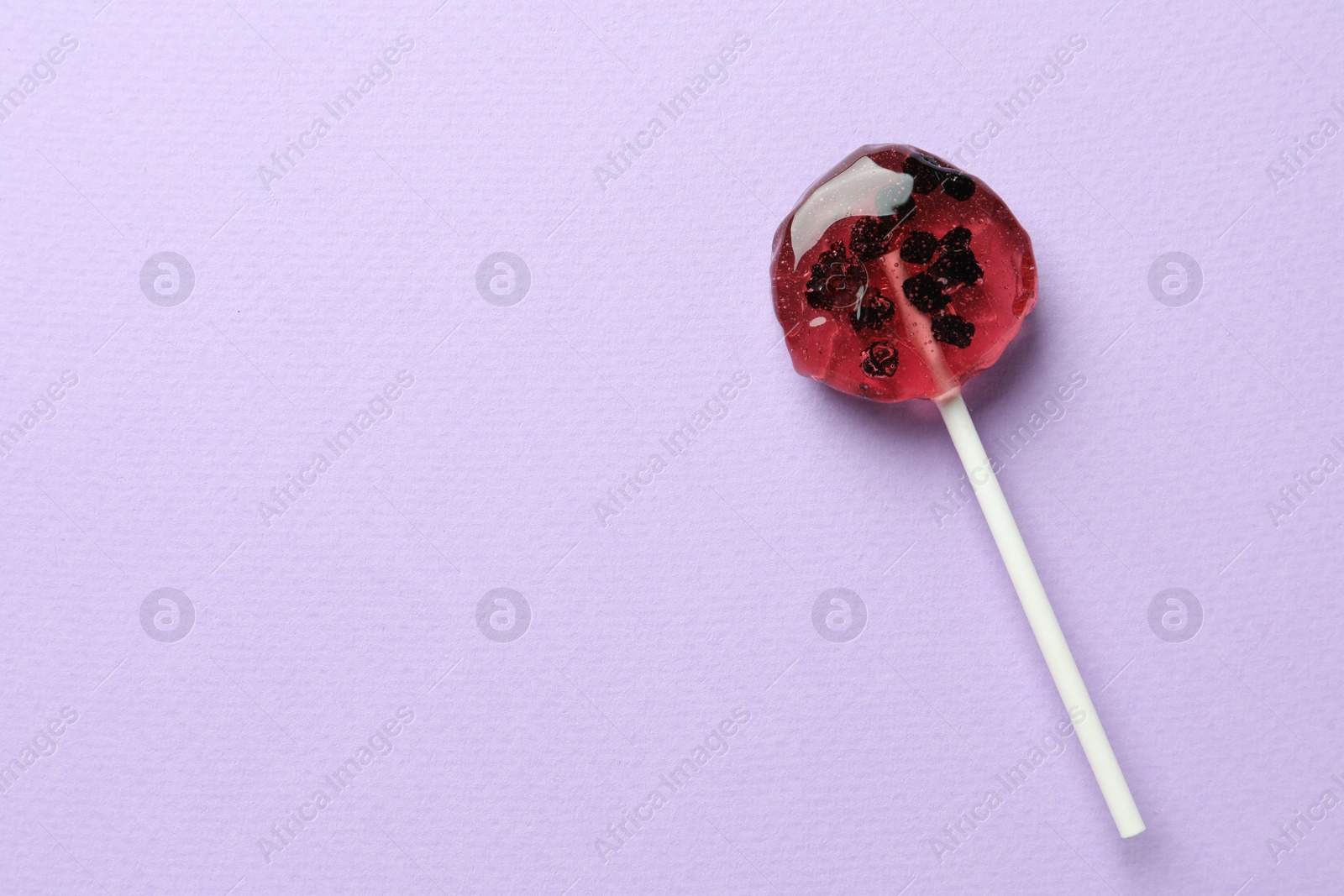 Photo of Sweet colorful lollipop with berries on lilac background, top view. Space for text