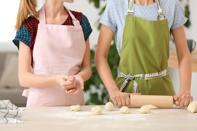 Mother and her daughter preparing dough at table, closeup