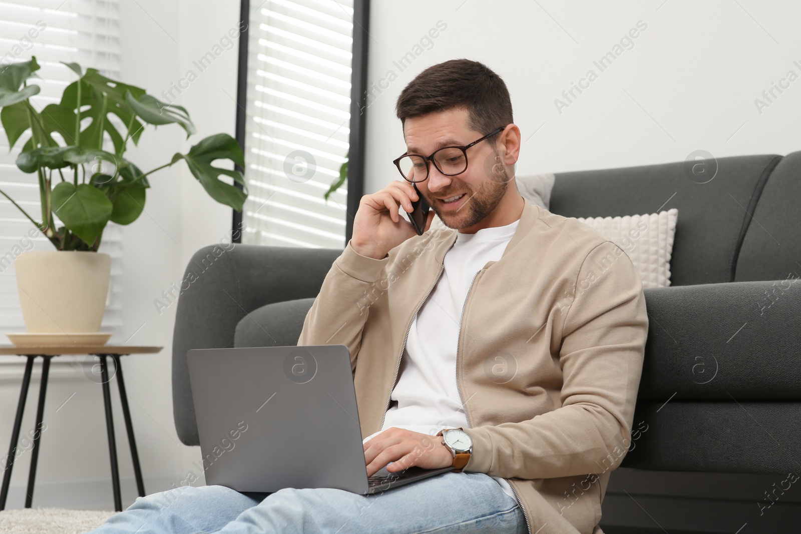 Photo of Man talking on smartphone while working with laptop at home