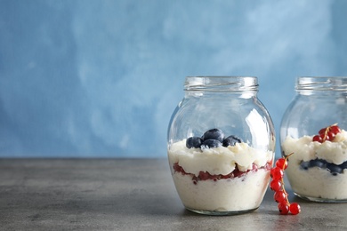 Photo of Creamy rice pudding with red currant and blueberries in jars on table. Space for text