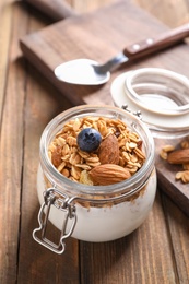 Jar with yogurt, nuts and granola on wooden table