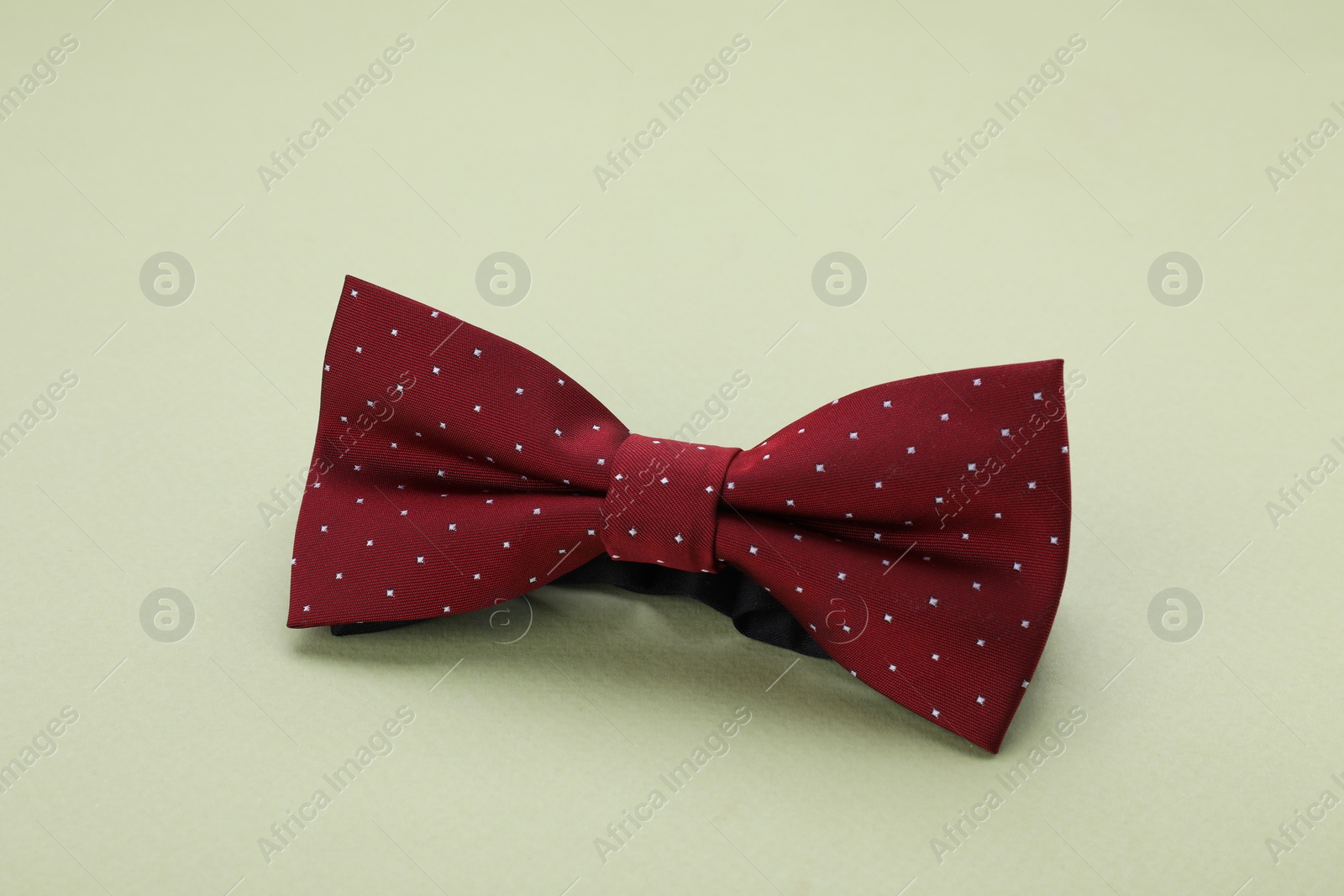 Photo of Stylish burgundy bow tie with polka dot pattern on pale green background