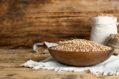 Photo of Bowl of wheat grains and spikes on wooden table. Space for text
