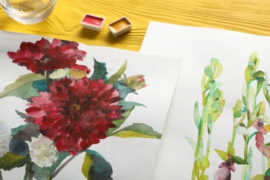 Photo of Beautiful floral pictures and watercolor paints on yellow wooden table