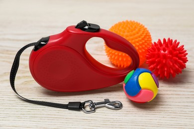 Red dog retractable leash and toys on white wooden background, closeup