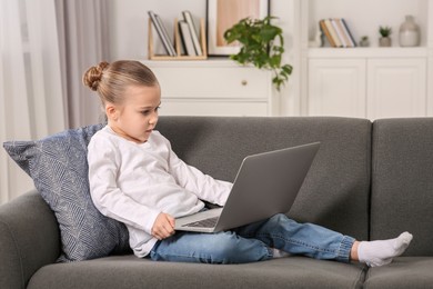 Photo of Little girl using laptop on sofa at home. Internet addiction