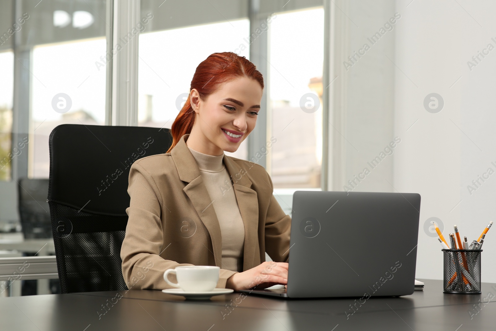 Photo of Happy woman working with laptop at black desk in office