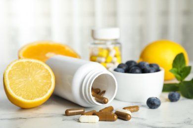 Photo of Bottle with vitamin pills, blueberries and lemon on white marble table