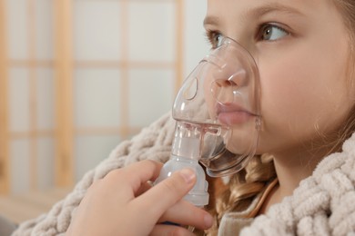 Photo of Little girl using nebulizer for inhalation at home, closeup