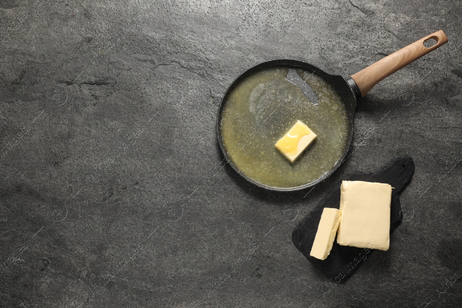 Photo of Melting butter in frying pan and dairy product on grey table, top view. Space for text