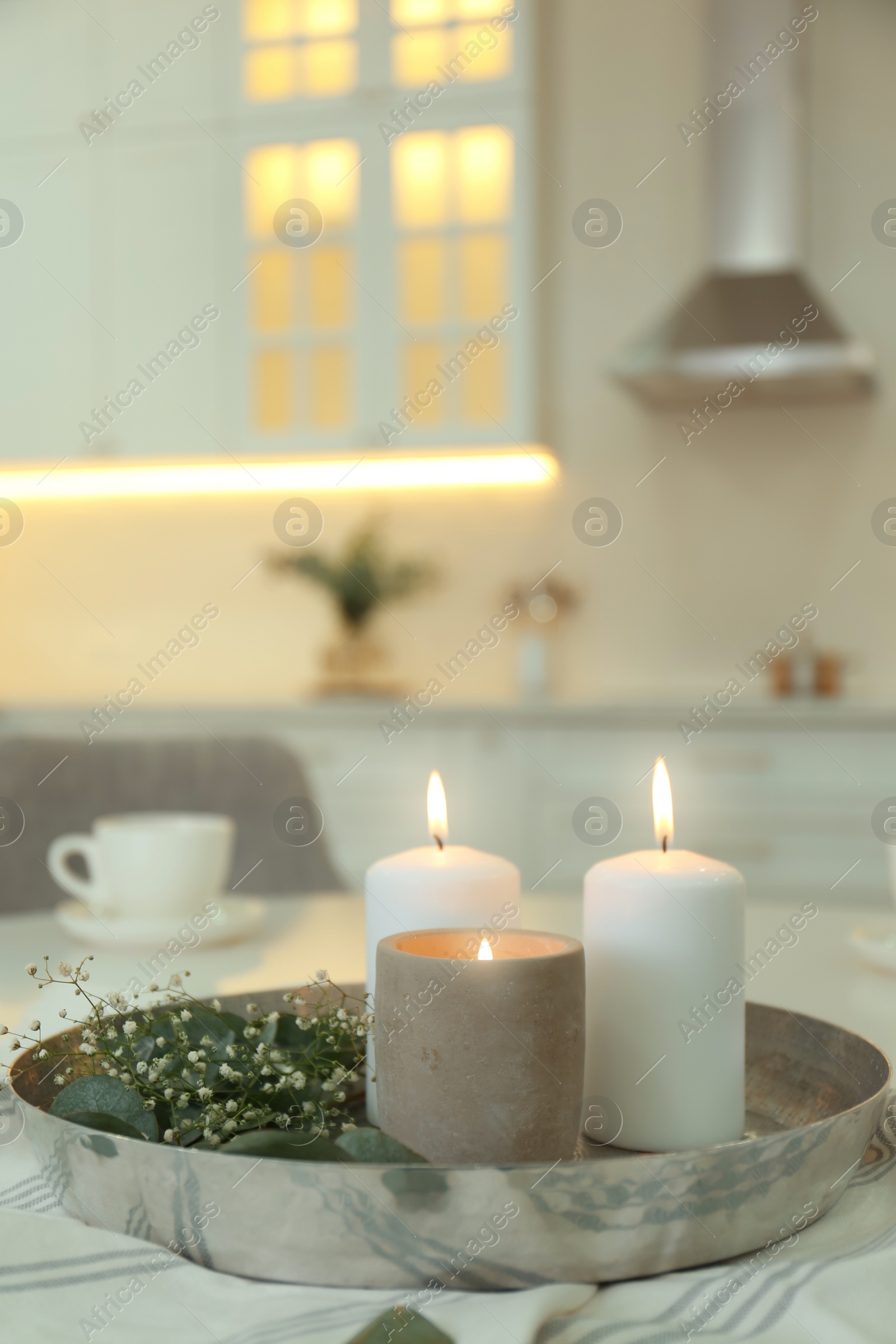 Photo of Beautiful eucalyptus branches, flowers and burning candles on napkin in kitchen, space for text. Interior element