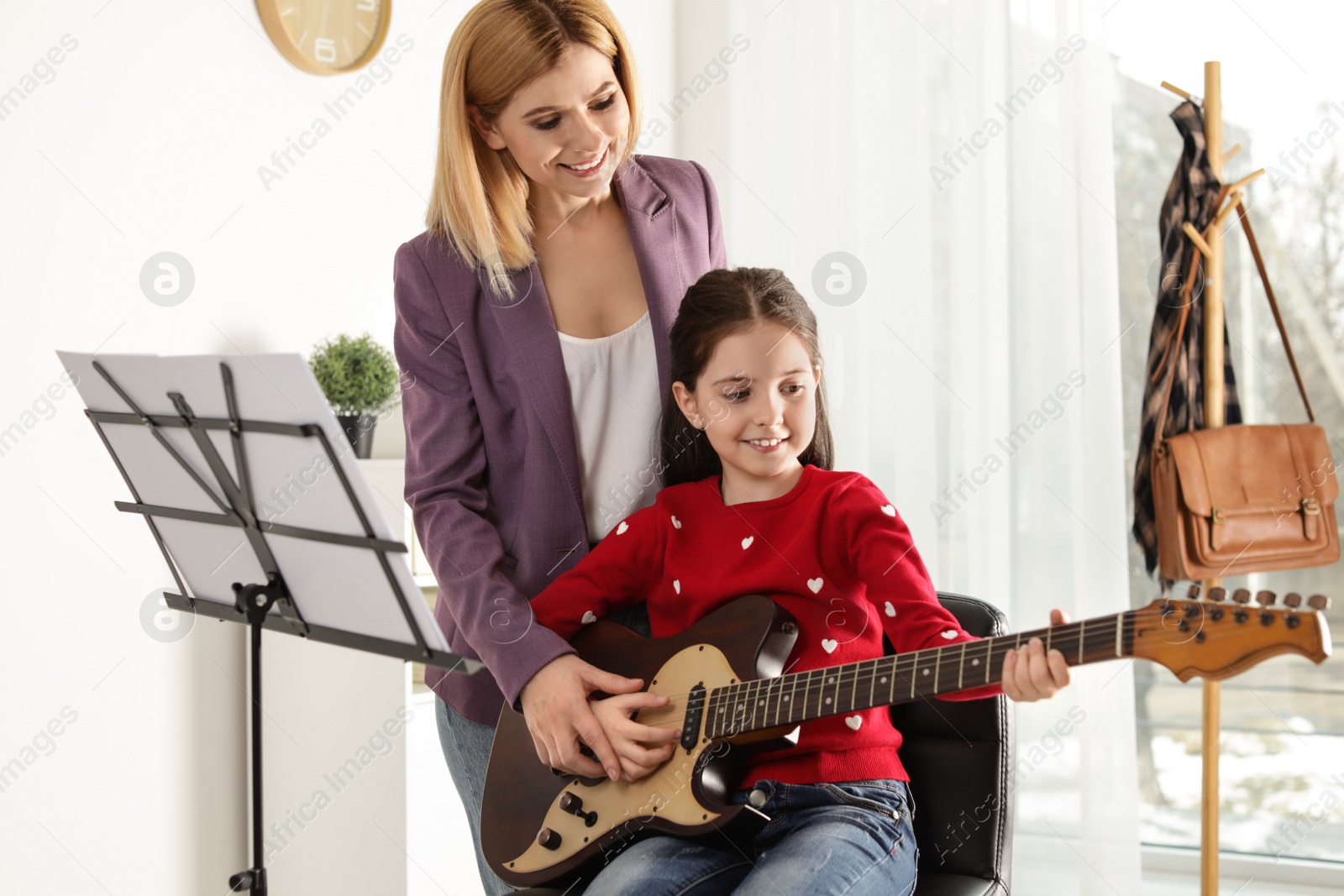 Photo of Little girl playing guitar with her teacher at music lesson. Learning notes