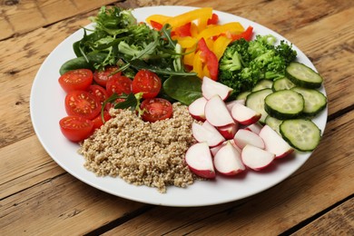 Photo of Vegetarian diet. Plate with tasty vegetables and quinoa on wooden table