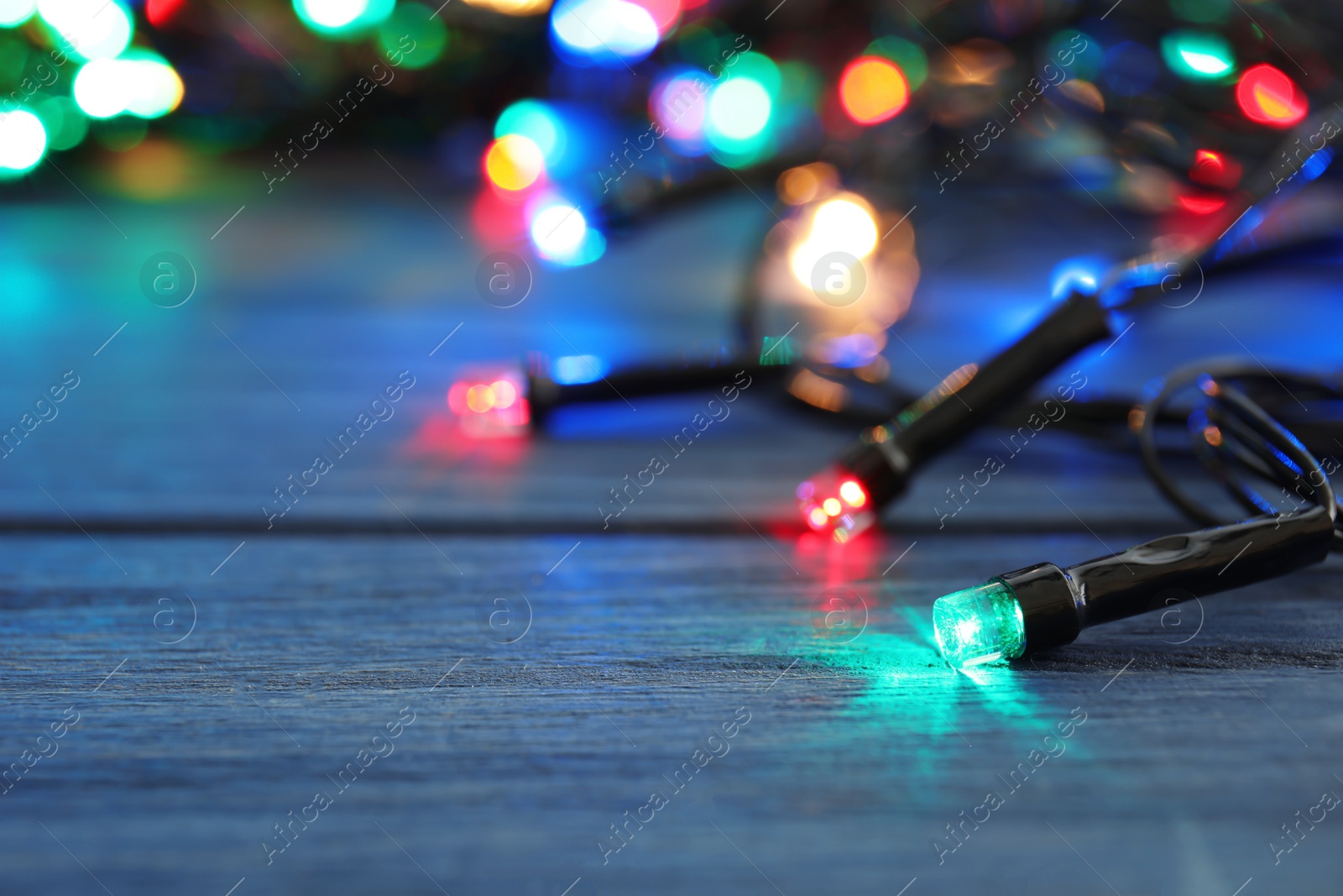 Photo of Glowing Christmas lights on wooden table, closeup