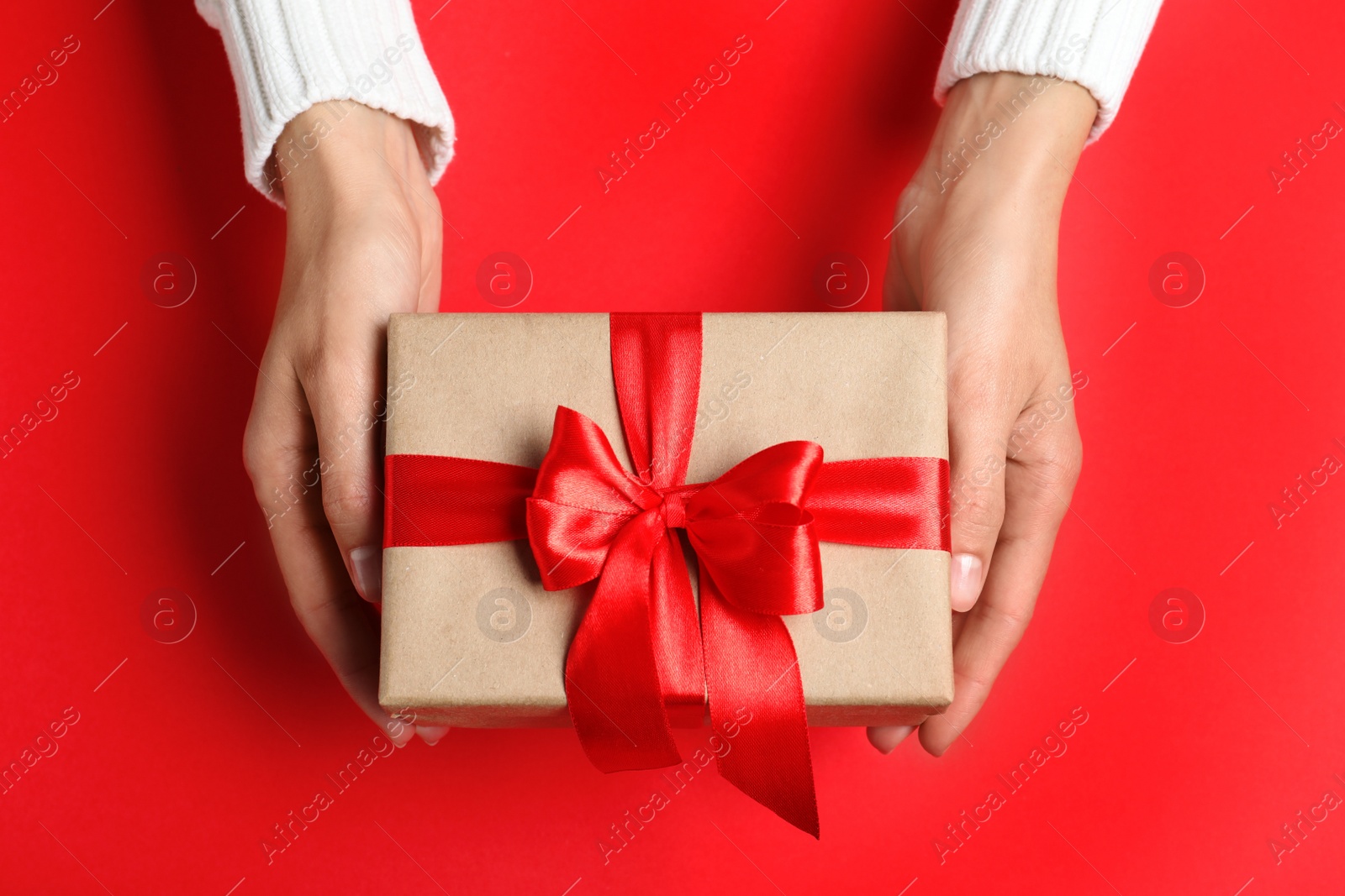 Photo of Woman holding Christmas gift on red table, top view