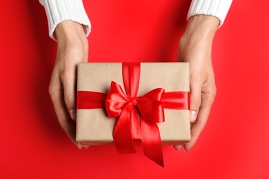 Woman holding Christmas gift on red table, top view