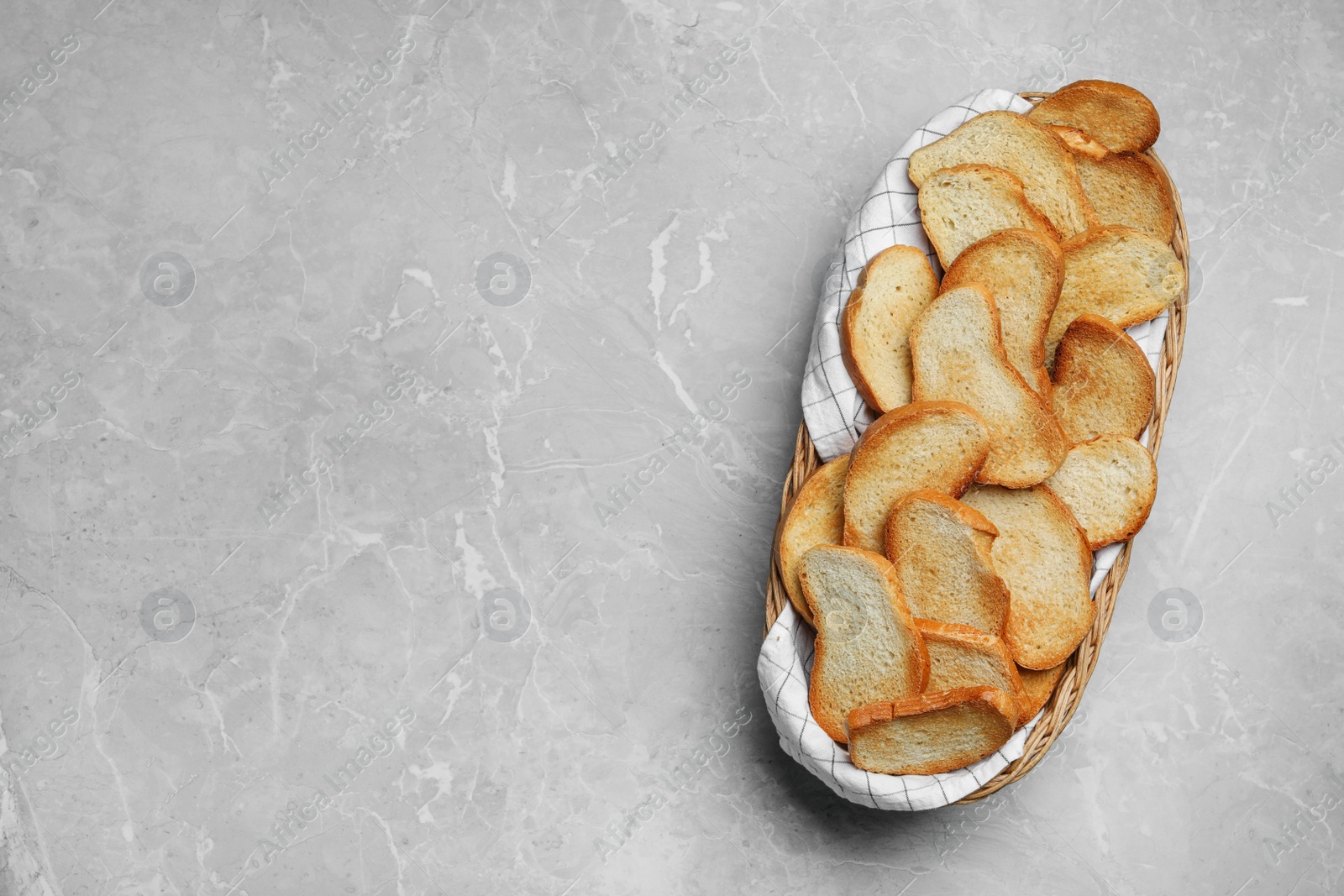 Photo of Basket with toasted bread on grey table, top view. Space for text