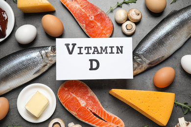 Paper with phrase VITAMIN D and fresh products on grey table, flat lay