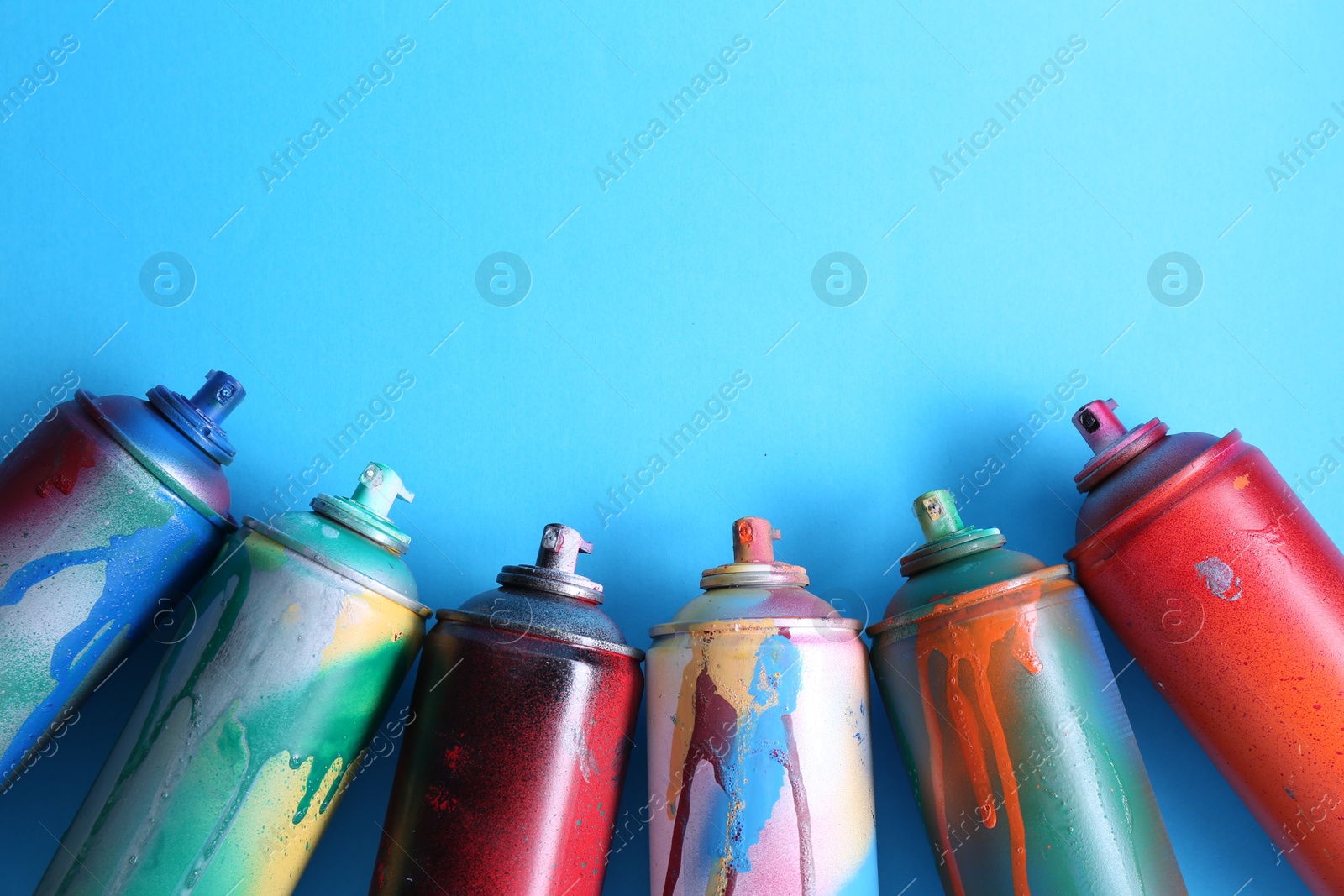 Photo of Many spray paint cans on light blue background, flat lay. Space for text