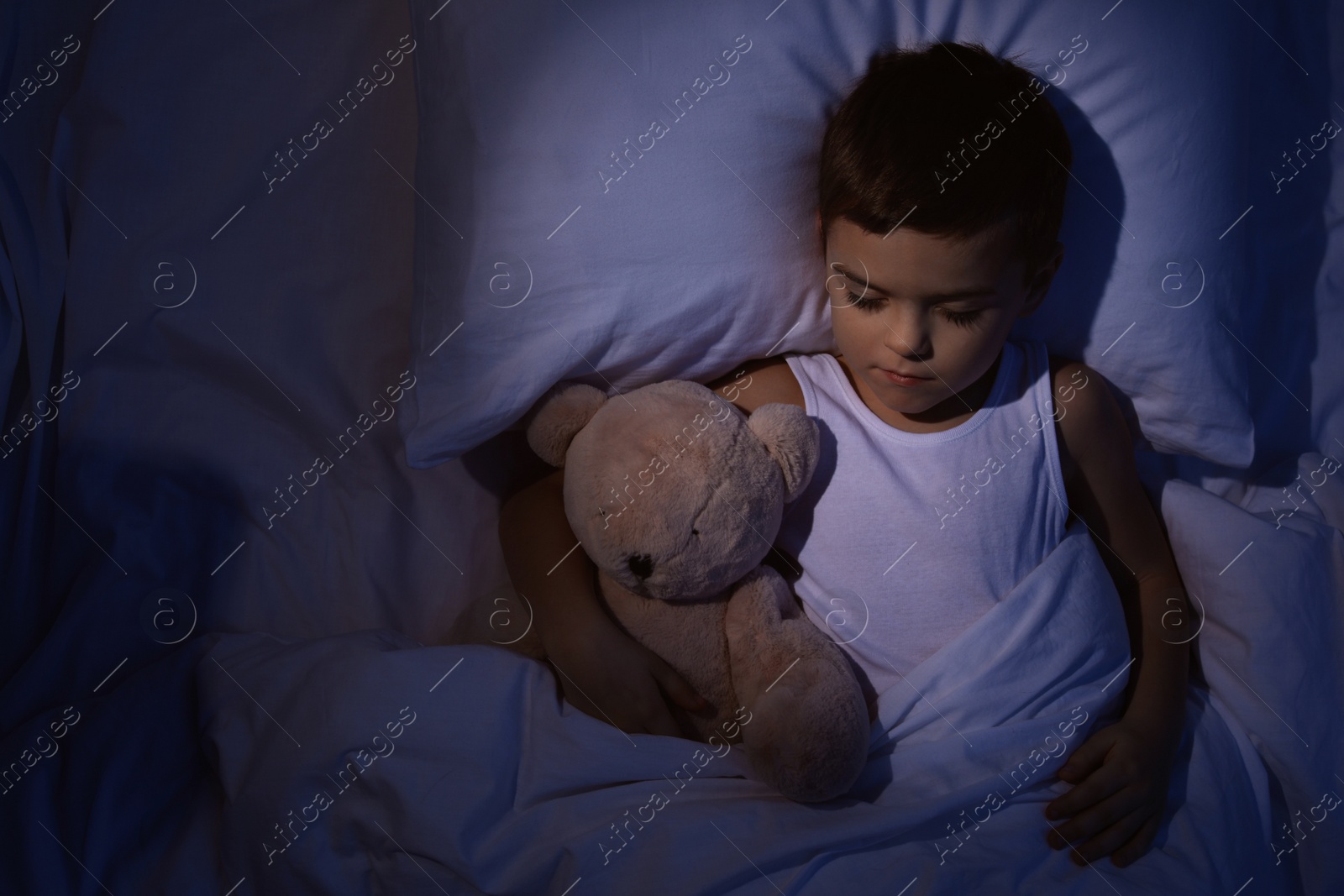 Photo of Little boy sleeping with teddy bear at home, top view. Bedtime