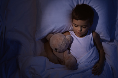 Little boy sleeping with teddy bear at home, top view. Bedtime