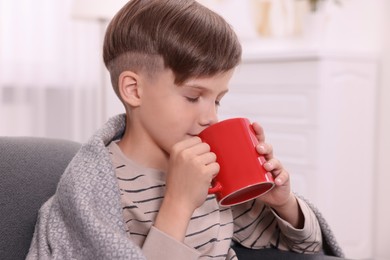 Cute boy drinking from red ceramic mug on sofa at home