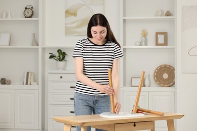 Young woman assembling furniture at table in room