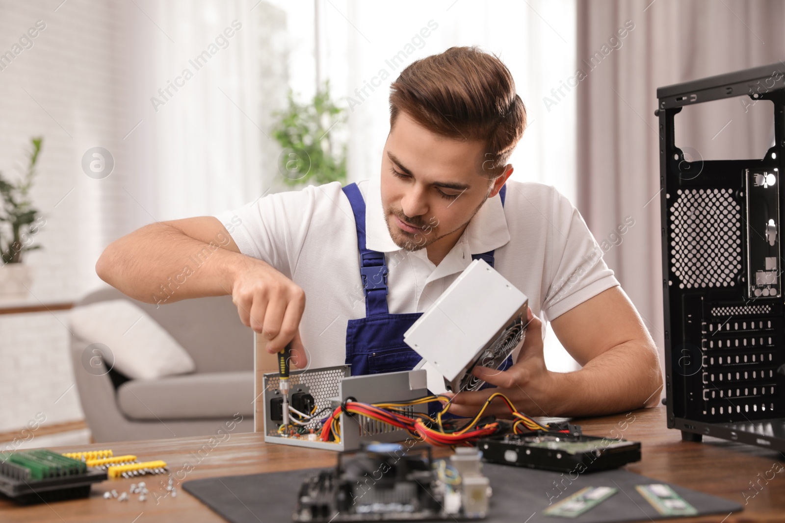 Photo of Male technician repairing power supply unit at table indoors